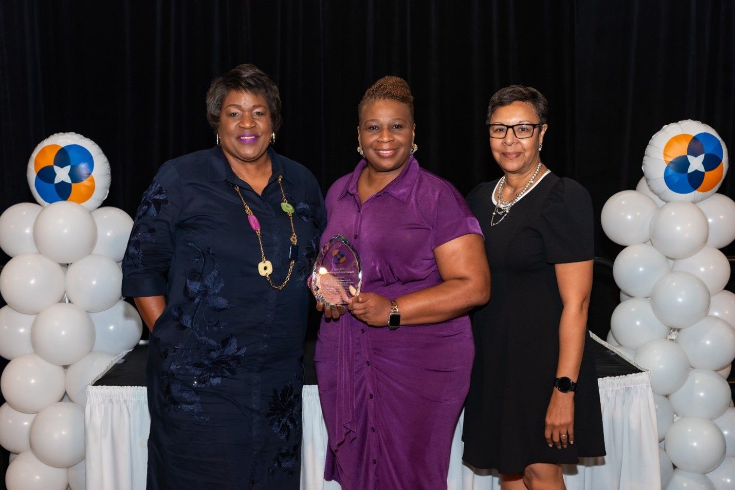 Three women standing together with the award winner in the middle