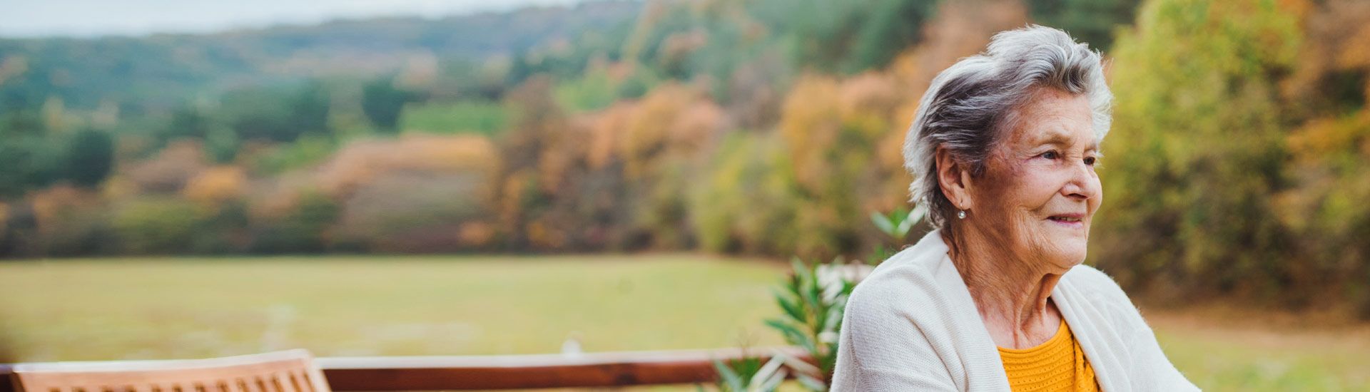 An elderly White woman outside on a deck looking at the landscape