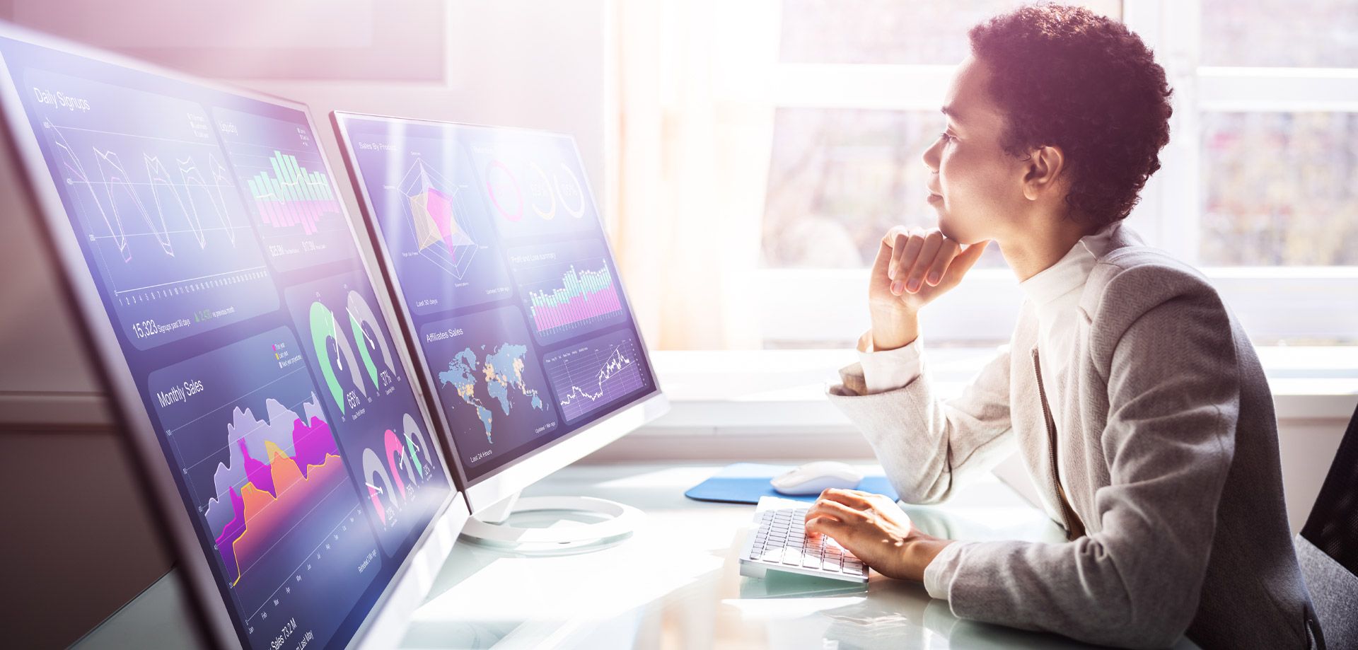 A woman using two large computer monitors to look at complex data