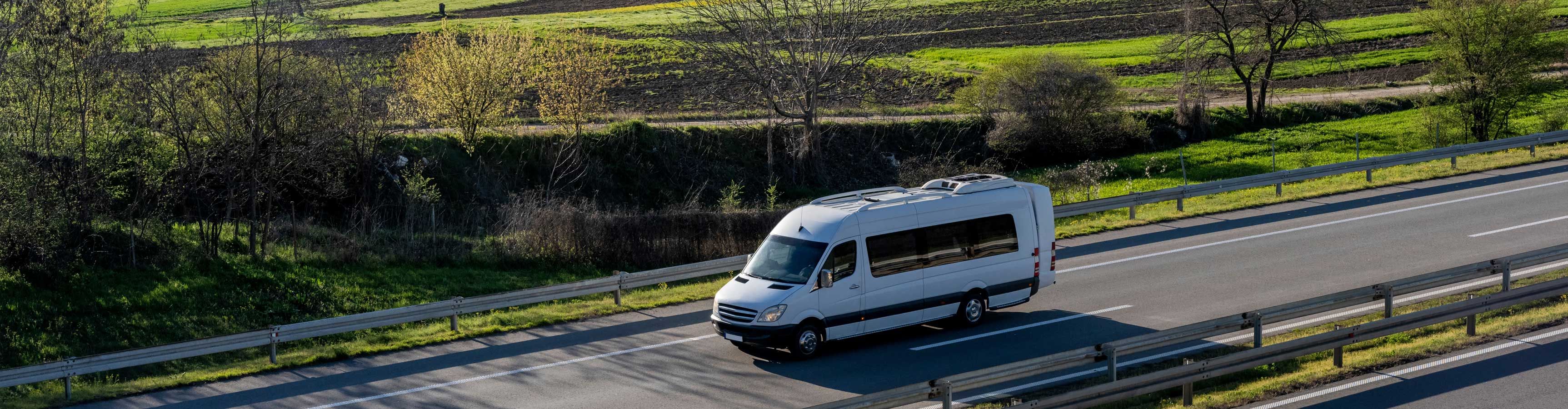 A white commuter van travels down a country road