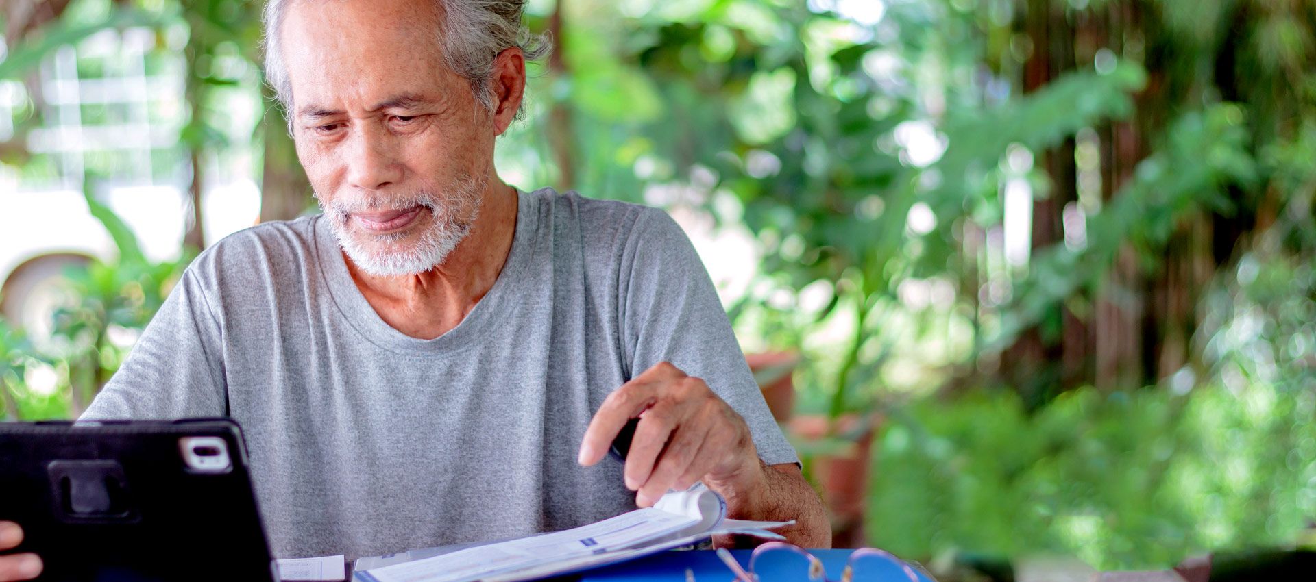 Asian man working outside at a table with a tablet and documents